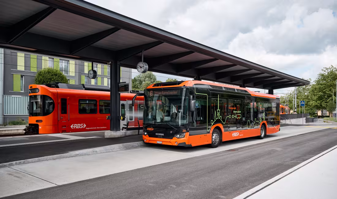 Moderner RBS Bus und Regionalzug an der Haltestelle Ittigen unter einem überdachten Perron, bereit für den Fahrgastbetrieb.
