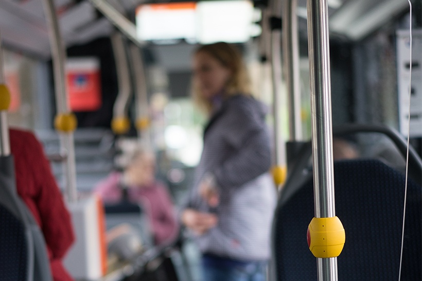 Ein Stopp-knopf in einem RBS Bus. Im Hintergrund ist verschwommen eine Frau mit Kinderwagen zu erkennen